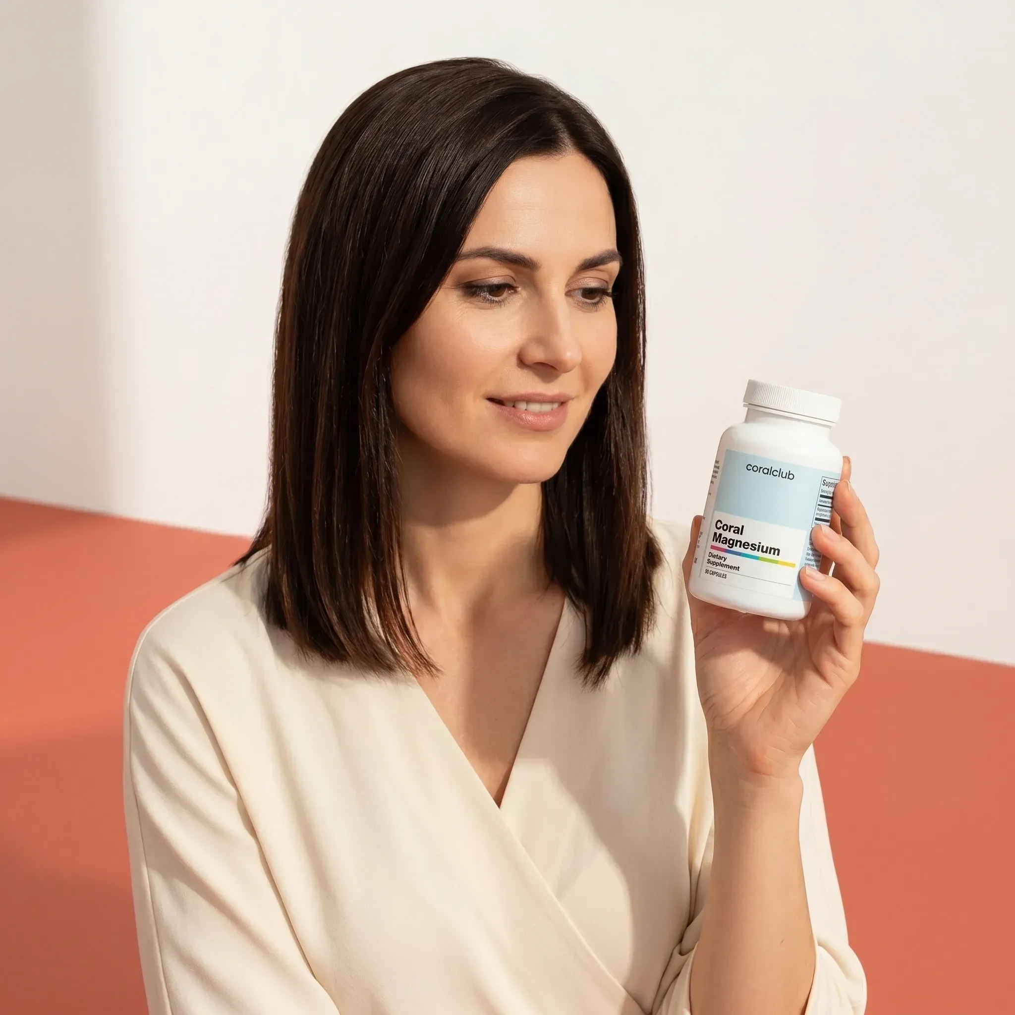 Woman holding Coral Magnesium supplement bottle in a modern, minimalistic lifestyle setting.