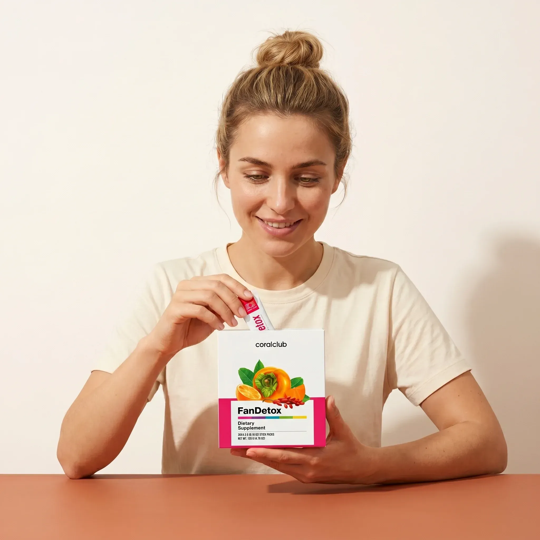Woman enjoying FanDetox supplement in a lifestyle setting, holding a packet with fruit visuals.