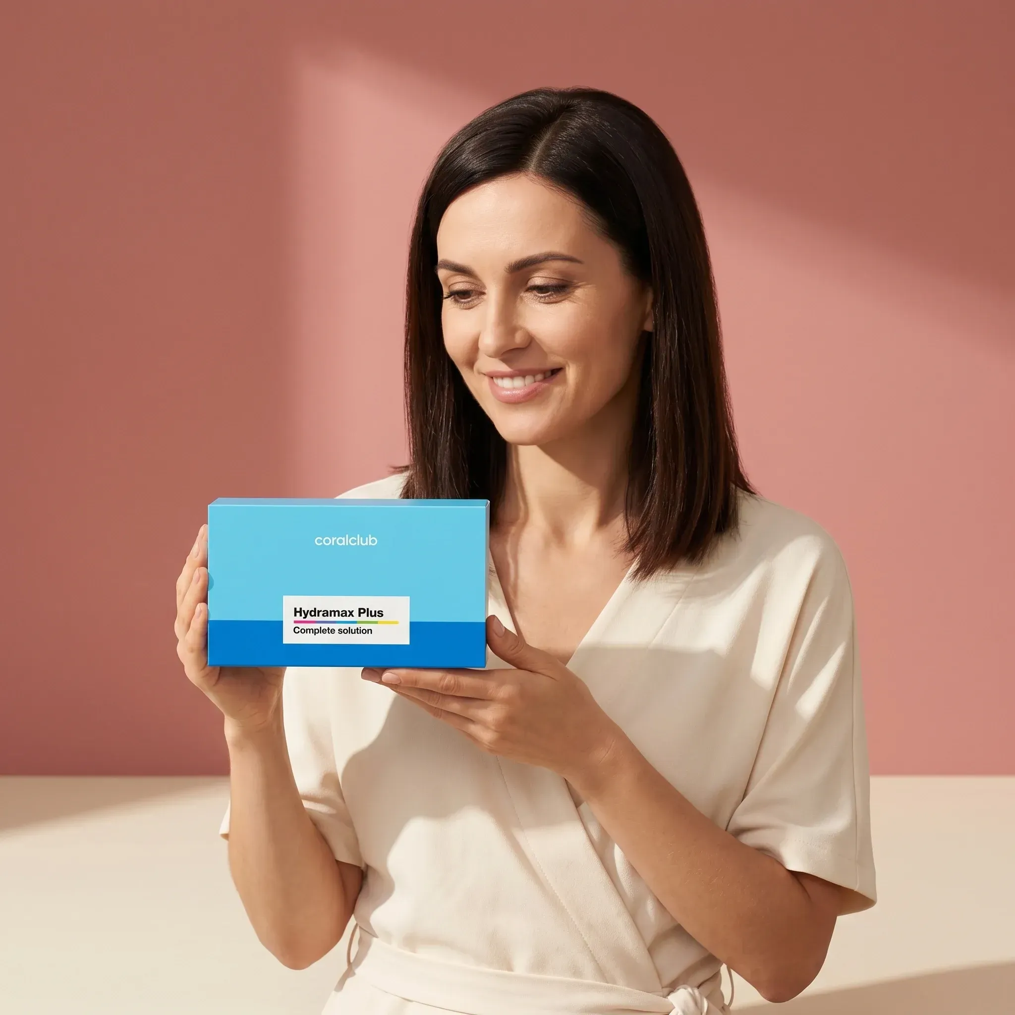 Woman holding HydraMax Plus box in a lifestyle setting with a soft pink background.