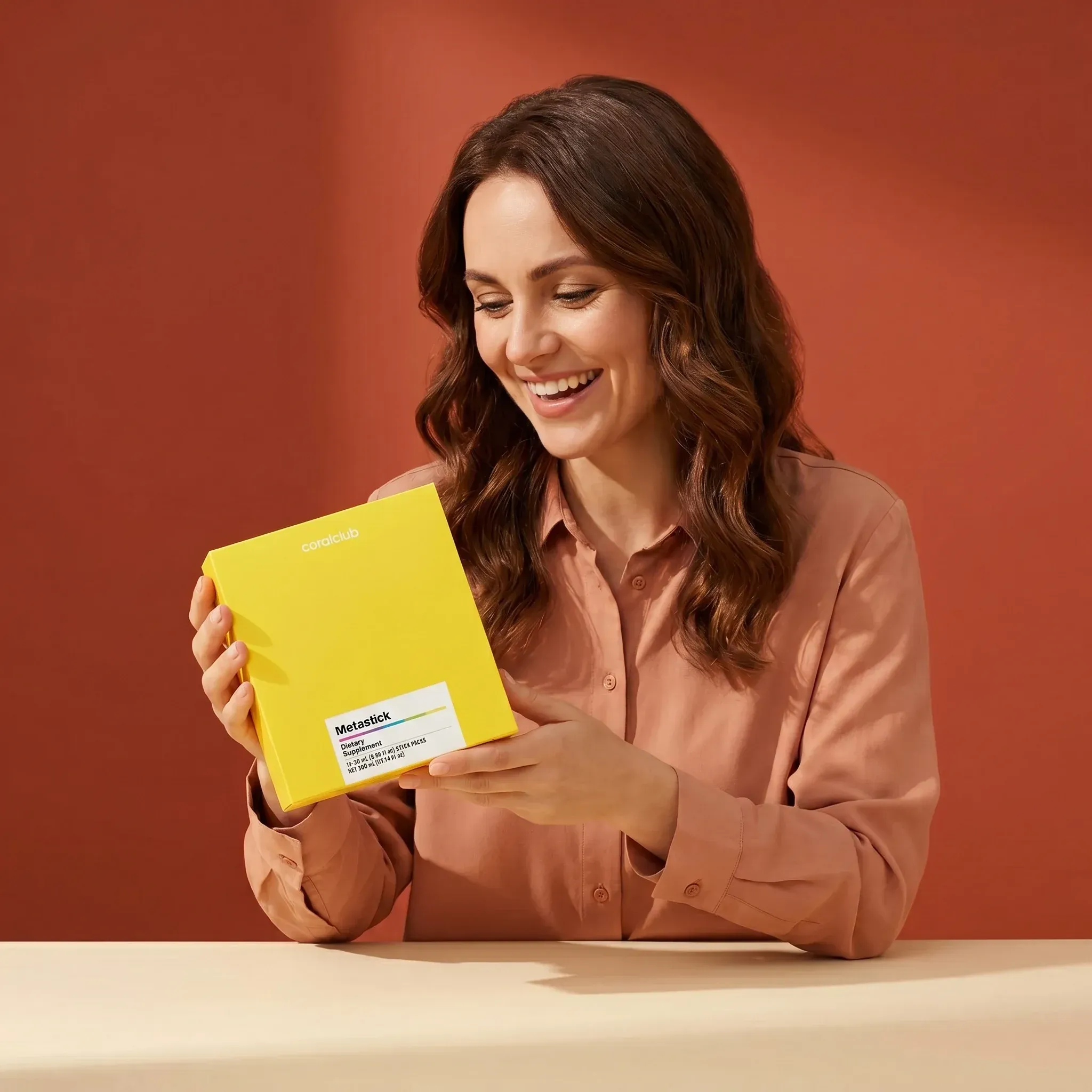 Woman smiling while holding Metastick product in a bright yellow box against a warm background.