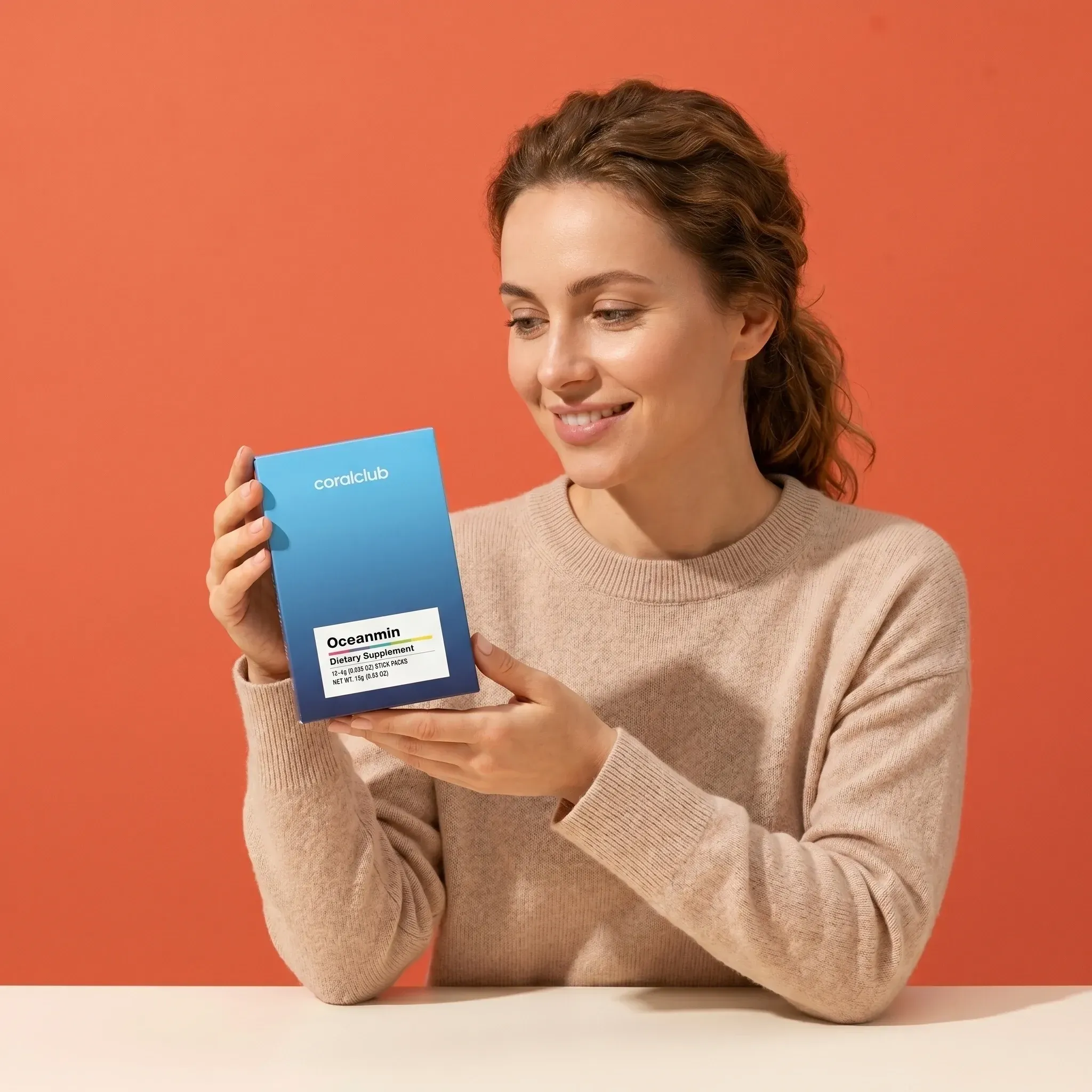 Woman holding Oceanmin supplement box against a vibrant orange background.